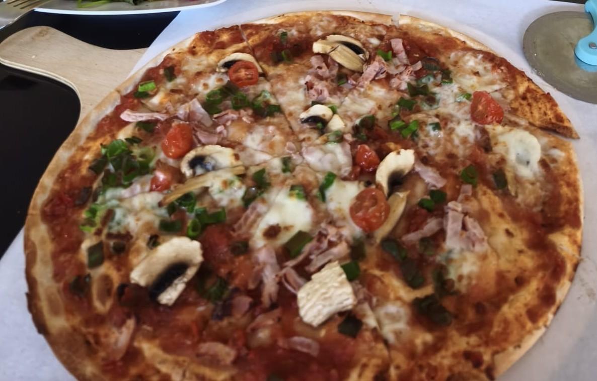 Frisch gebackener Flammkuchen mit Schinken, Champignons, Kirschtomaten und Frühlingszwiebeln